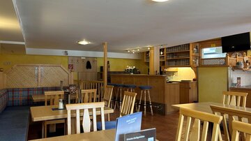 A cozy restaurant with wooden tables and chairs. The bar is clearly visible and the walls are painted in warm colors.