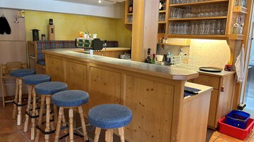 A cozy bar with wooden shelves and glasses. There are several stools with blue seat cushions and an inviting atmosphere.