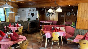 A cozy restaurant with wooden walls and rustic furniture. The tables are decorated with red tablecloths and well set.