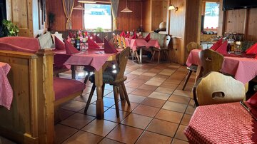 A cozy restaurant with wooden paneling and red checkered tablecloths. The tables are set for guests and there is an inviting atmosphere.