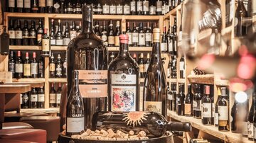 A selection of wines in a wine shop. Several large wine bottles are standing on a wooden barrel, surrounded by wine shelves.