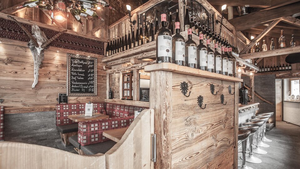 A cozy restaurant with wood decor and a bar. The bottles are on a wooden shelf, and there are seating options for guests.