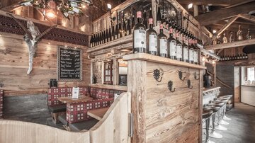 A cozy restaurant with wood decor and a bar. The bottles are on a wooden shelf, and there are seating options for guests.