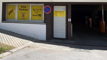 An entrance door to a postal partner with yellow advertising signs. The area is well lit and includes a parking lot.