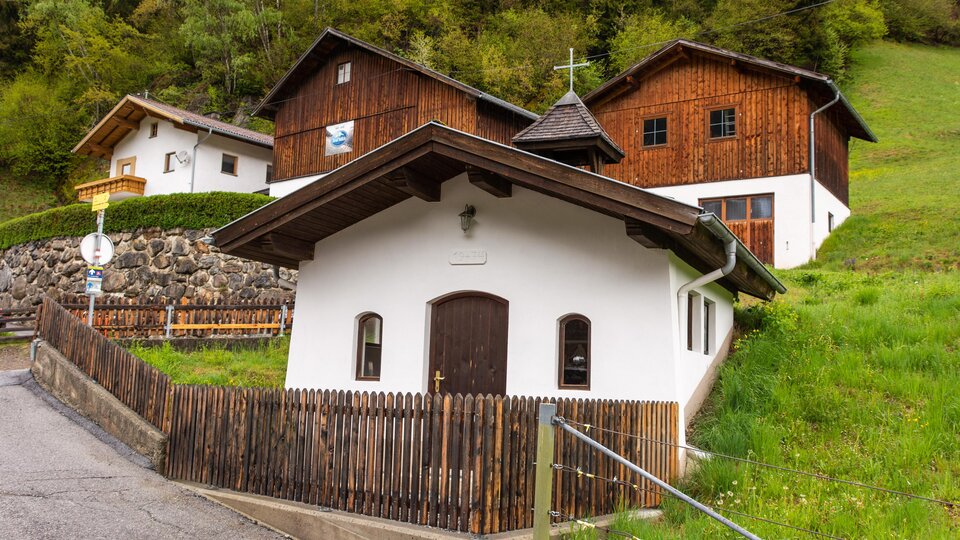 A picturesque village with traditional wooden houses and a small church. Surrounded by green meadows and trees. | © Bernhard Gruber – Photography