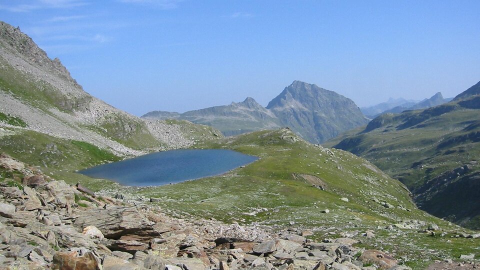 A picturesque mountain landscape with a clear blue lake. In the background, majestic mountains rise under a blue sky.