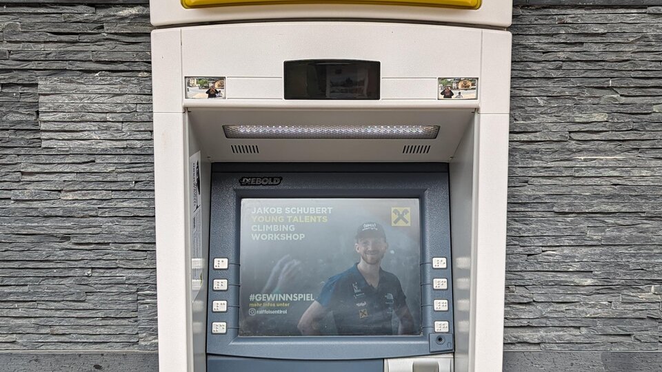 An ATM on a wall. It displays a simple user interface with a card and a screen.