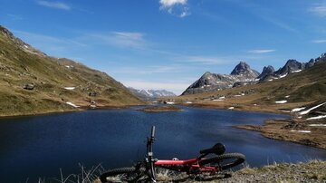 Eine atemberaubende Landschaft mit einem klaren See und Bergen im Hintergrund. Ein Fahrrad liegt am Ufer des Sees.