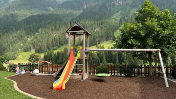 A playground surrounded by beautiful mountains. The slide is colorful and there is a swing for children.