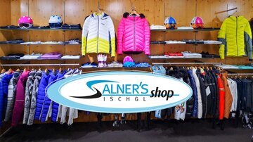 A ski shop with colorful jackets and accessories can be seen. The clothing is neatly arranged on shelves, and there are also helmets in various colors.