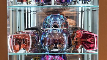 A large selection of colored ski goggles in a glass case. The goggles have different designs and mirrored lenses.