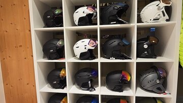 A shelf with various helmets, neatly arranged in boxes. Some helmets are black, others are white and have colorful patterns.