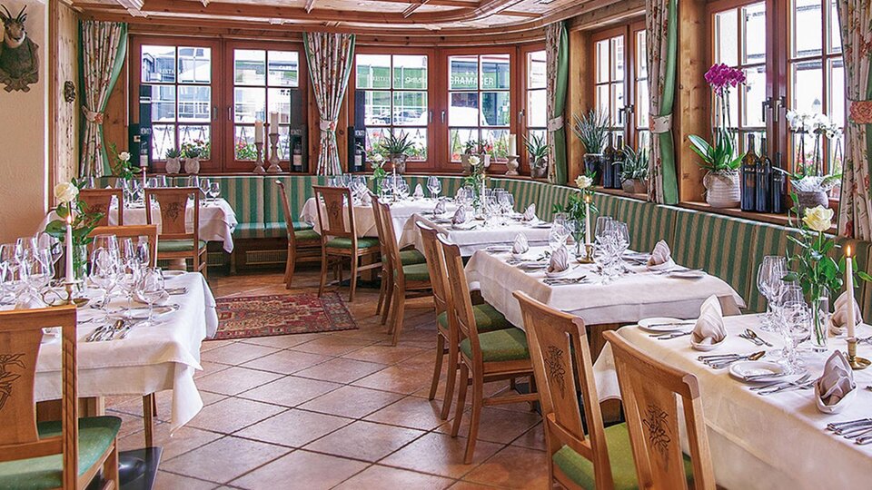 An elegant restaurant with wooden furniture and a cozy atmosphere. The tables are festively decorated with glasses and flowers.