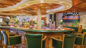 An elegant bar with a curved counter and cozy green bar stools. The warm wooden ceiling and decorative plants create an inviting atmosphere.