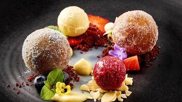 An artfully arranged dessert plate with three filled spheres in different flavors. Surrounded by colorful fruits and decorative elements.