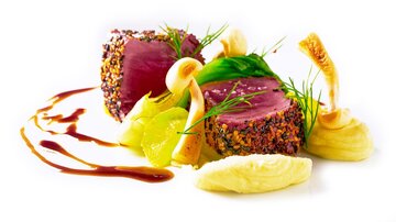An artfully arranged dish with tender meat, surrounded by colorful vegetables and a fine sauce. The presentation is elegant and inviting.
