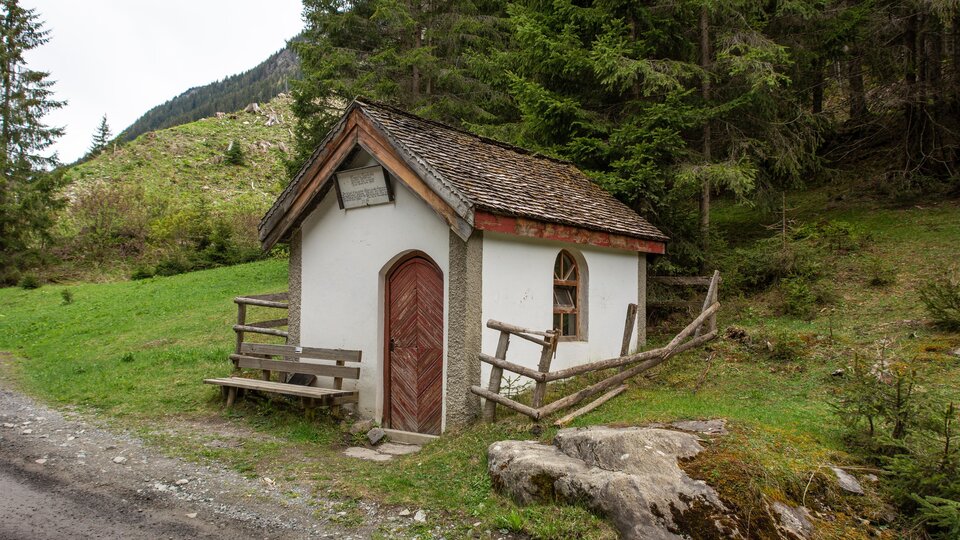 A small, picturesque cabin stands in the midst of a green landscape. Surrounded by trees and mountains, it offers a tranquil atmosphere. | © Bernhard Gruber – Photography