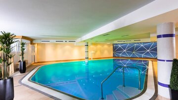 An elegant indoor pool with blue water and modern design elements. The surroundings are bright and inviting, with plants for a relaxed atmosphere.