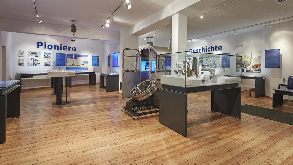 A modern exhibition room with wooden floors.  
Display cases and information about pioneers and history are mounted on the walls.