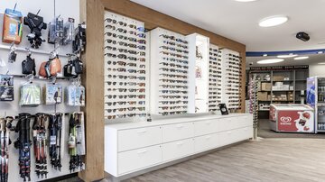 A store with a large selection of sunglasses on the wall. On the left side, various accessories such as straps and holders can be seen.