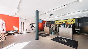 Ein modernes Sportgeschäft mit Ski- und Outdoor-Ausrüstung. Die Wände sind bunt gestaltet, und es gibt eine Verkaufsfläche mit verschiedenen Markenprodukten.