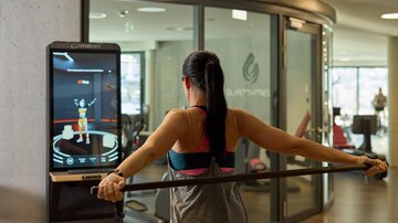 A person is training in the gym with a digital monitor. The monitor displays exercises while the person works with a resistance band.
