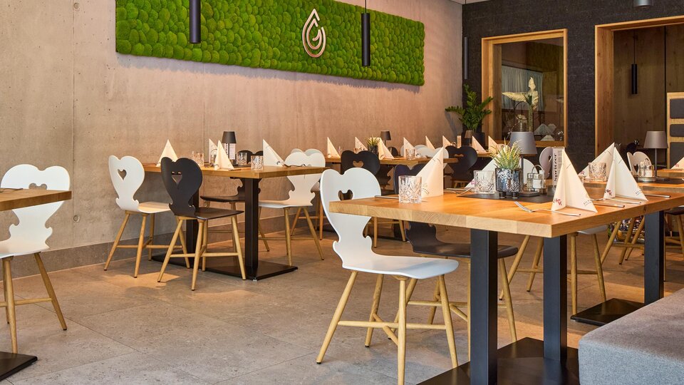 A modern restaurant with stylish tables and chairs.  
On the wall, there is a vibrant plant wall that creates an inviting atmosphere.