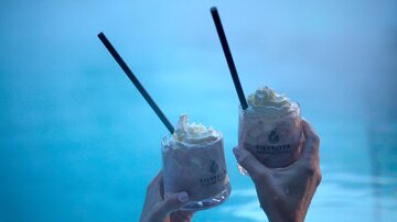 Zwei Cocktails mit Sahne in Händen, die über einem blauen Pool gehalten werden. Die entspannte Atmosphäre lädt zum Genießen ein. | © Silvrettaseilbahn AG