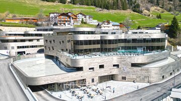 Ein modernes Hotelgebäude in einer bergigen Umgebung. Umgeben von grünen Wiesen und traditionellen Chalets.
