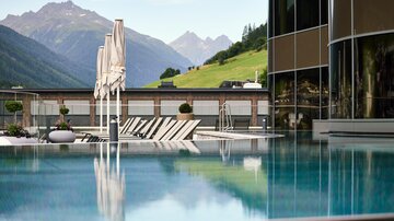 Ein schöner Infinity-Pool mit Blick auf grüne Berge. Sonnenschirme und Liegen laden zum Entspannen ein.