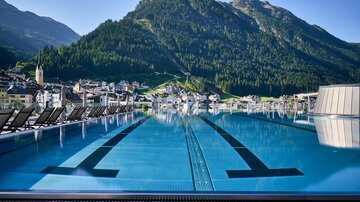 Ein stilvoller Infinity-Pool mit Blick auf grüne Berge. Im Hintergrund ist eine malerische Stadt zu sehen.