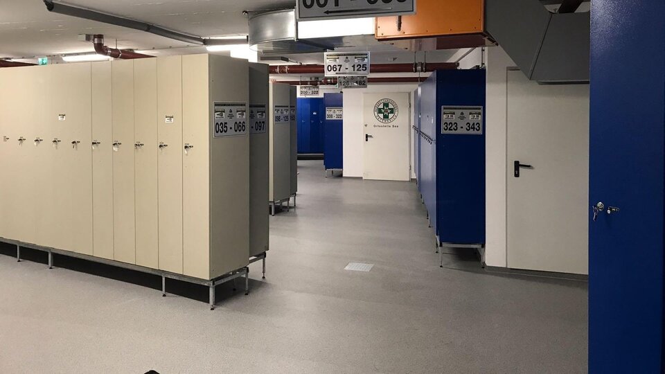 A modern changing area with numerous lockers. The walls are painted blue and the lighting is bright.