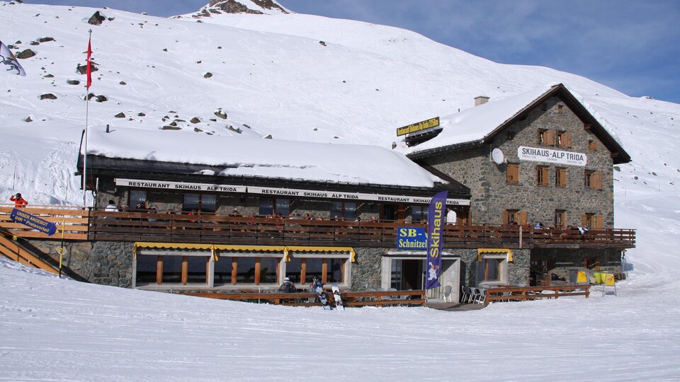 A cozy mountain house in the snow, surrounded by a winter landscape. The facade is made of stone with a large balcony and sunny terraces.