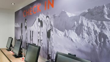 A modern check-in area with multiple computers. In the background, skis are depicted against a snowy mountain landscape.