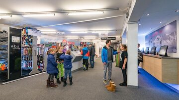 A ski rental shop with skis and equipment in a modern store. Some customers, including children, are busy in the shop.