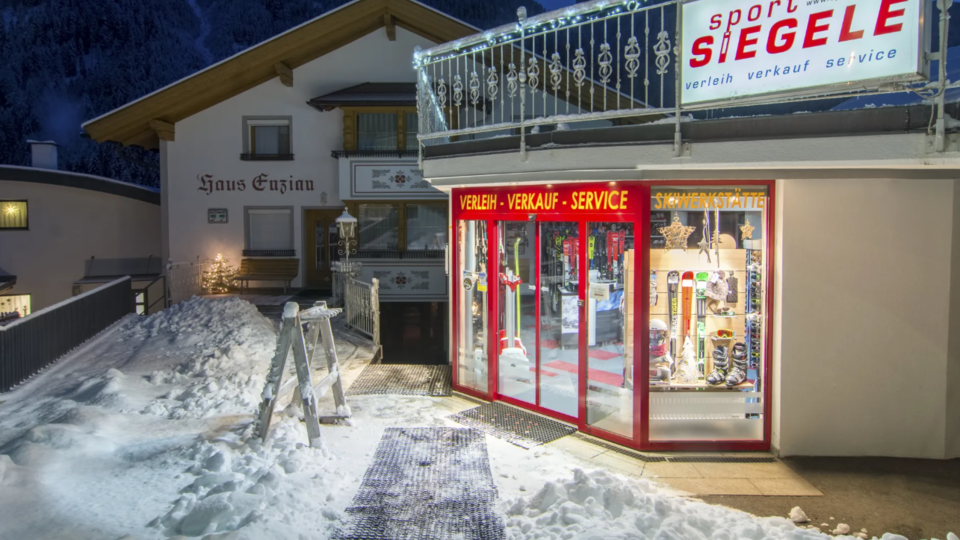 A sports store with large windows, located in a snowy environment at twilight. The building has a cozy atmosphere and is situated in the mountains.
