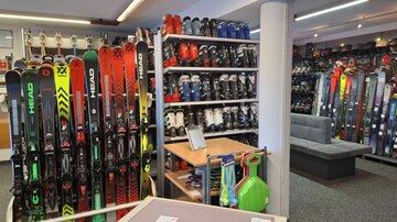 A store for winter sports equipment with many skis and ski boots. The shelves are well stocked and there is a cozy seating area.