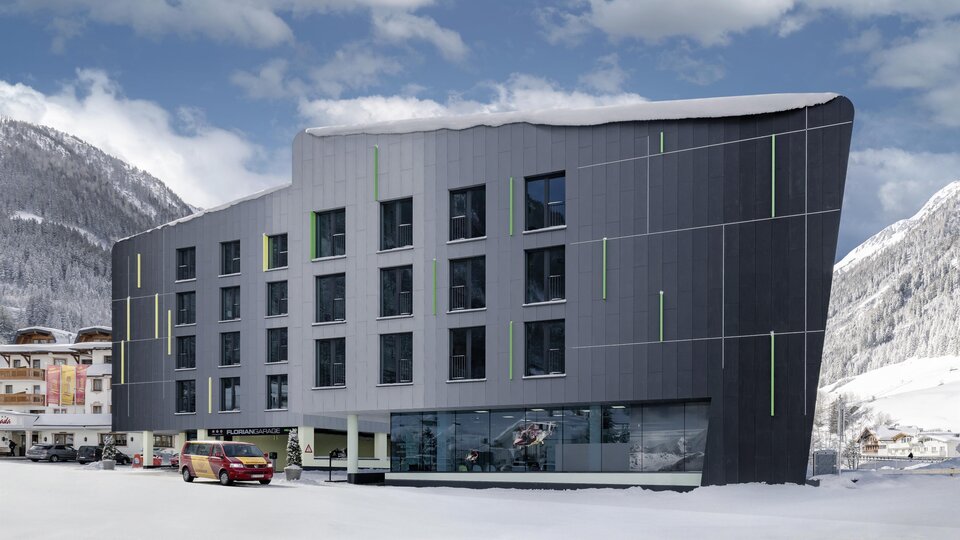 A modern hotel building in a snow-covered mountain valley. The facade is stylish and eye-catching, surrounded by a wintry landscape.
