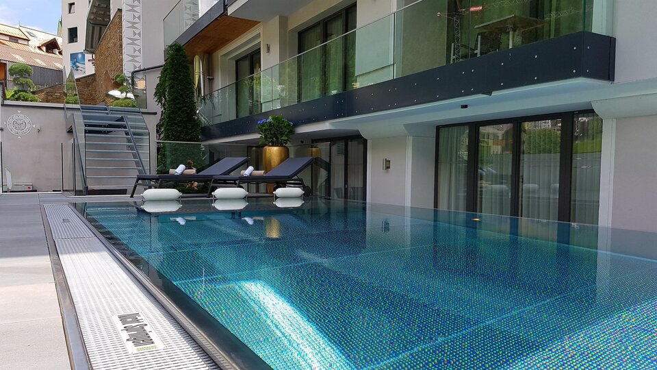 An elegant swimming pool with crystal clear water and modern loungers. In the background, there is a stylish building with large windows and plants.