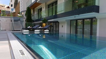 An elegant swimming pool with crystal clear water and modern loungers. In the background, there is a stylish building with large windows and plants.