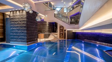 An elegant spa area with a clear blue pool and stylish design. The lighting creates a relaxing atmosphere.