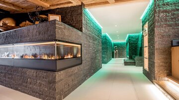 A modern interior with stone walls and soft, green light. In the background, an elegant fireplace is visible, creating a cozy atmosphere.