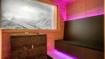 A modern wellness area with a stone bench and soft, colorful lighting. In the background, there is a large picture of snow-covered mountains.