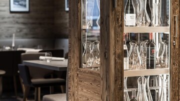 An elegant dining area with a wooden glass rack. The decor is modern and stylish, with cozy tables.