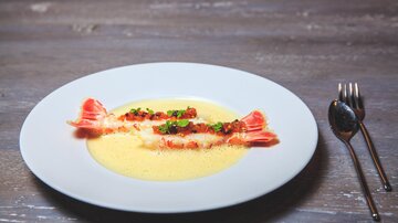 An elegant dish on a white plate with two stuffed dumplings and a creamy sauce. The dish is garnished with fresh herbs and a red sauce.