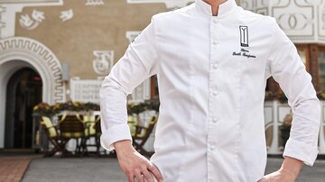 A chef stands confidently in front of the Yscla inn. The background shows the well-decorated facade of the restaurant.