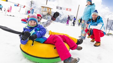A group of children and adults is having fun in the snow. They are riding on tires and laughing in the wintry landscape.