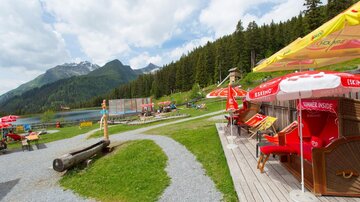 Ein schöner Aussichtspunkt am See mit Liegestühlen und Sonnenschirmen. Im Hintergrund sind Berge und Wälder zu sehen.