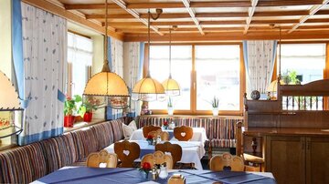 A cozy restaurant with wooden furniture and colorful benches. Large windows let in plenty of light and create an inviting atmosphere.