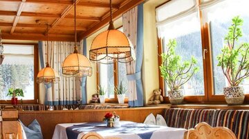 A cozy restaurant with wooden elements and warm lighting. There are plants and decorated tables with appealing seating.